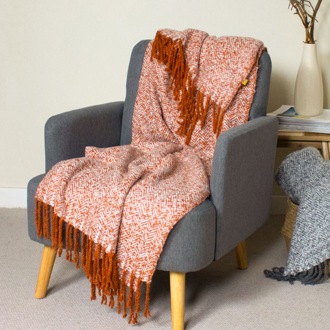 a rust coloured wool throw with twisted tassels thrown on a blue armchair.