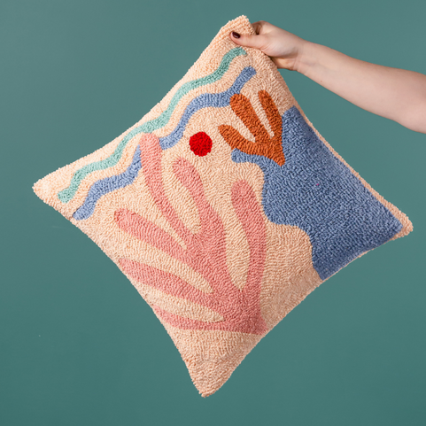 a peach coloured cushion with a coral ocean design being held in frame.