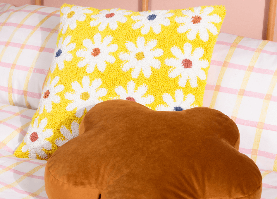 a yellow daisy knitted cushion and a ginger velvet flower cushion lying on white, pink and yellow geometric patterned bedding.