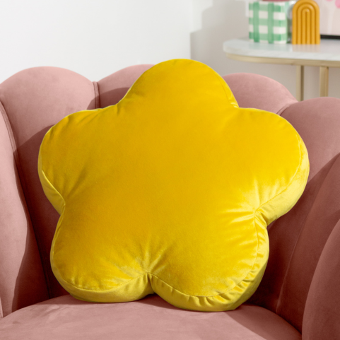 a bright yellow flower shaped velvet cushion, sitting on a blush pink velvet chair.