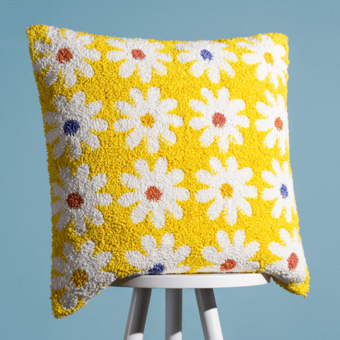 a yellow tufted cotton cushion designed with white daisies that have yellow, rust orange and pastel violet centres. 