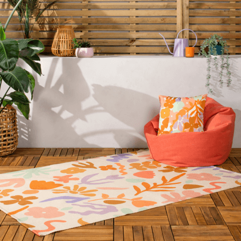 a flatweave polyester indoor/outdoor rug in a neutral off-white hue, designed with a multicoloured abstract floral pattern in pastel tones of orange, pink, violet and mint green.