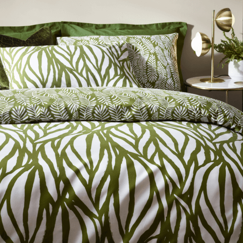 an olive green duvet cover set with a linear leaf pattern, dressed on a bed with a table lamp and a potted plant on a side table in the background.