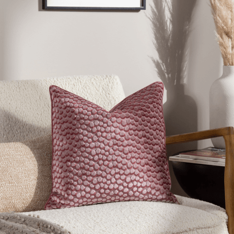 a plaster pink velvet cushion with an abstract circle 3D design, sitting on a textured cream chair with a coordinating nougat cushion.