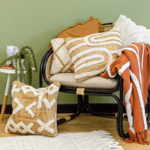 A selection of woven cushions with geometric tufted designs, piled on an armchair with an orange tufted throw.