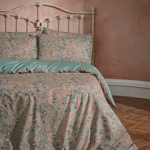 a pink bedroom with a romantic, ornate, metal bed frame. The bedding on the bed is pink and mint green floral pattern. 