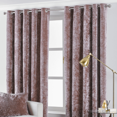 a pair of pink crushed velvet eyelet curtains open at a window with an anglepoise lamp in front of it. 