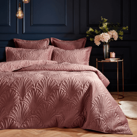 a dramatic bedroom with dark walls and blush pink bedding with a quilted velvet pattern.