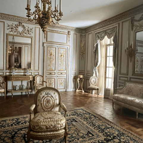 an ornate room that might look at home in the palace of Versailles. gold ornate chairs, lots of panelling, crowning and plaster work. there's a big rug and a gold chandelier too.