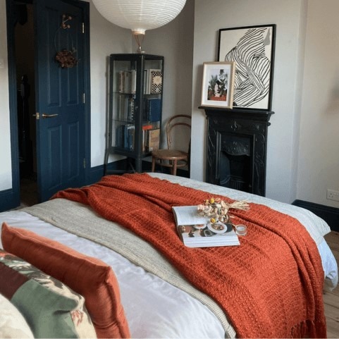 a bed with orange and white bedding. there's a natural throw and an orange throw layered on the bottom. there's a tray and flowers on top of it. the walls of the bedroom are white, and the door is blue.