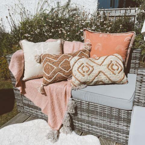 a grey outdoor sofa on a sunny day, layered up with jute cushions and a soft pink throw.