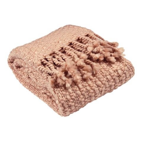 a knitted throw in blush pink. it has a loose knit and fringing