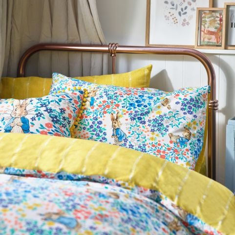 A bed with a metal bed frame and a blue and yellow ditsy floral duvet cover set. In the pattern you can see Peter Rabbit.  