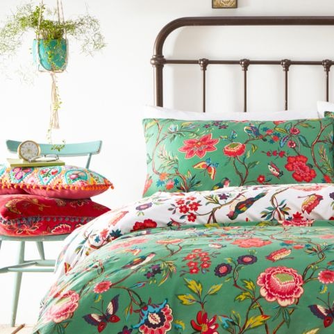 A bed with a green floral duvet cover set on it, featuring a bright flower pattern that includes birds and butterflies too.