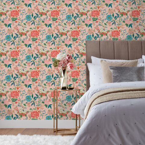 A bedroom with a pink floral patterned wallpaper with blue and pink flowers on. 