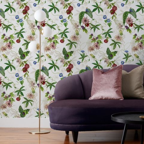 A living room with a floral patterned wallpaper with intertwining figs, passionflowers and foliage on a pale background.