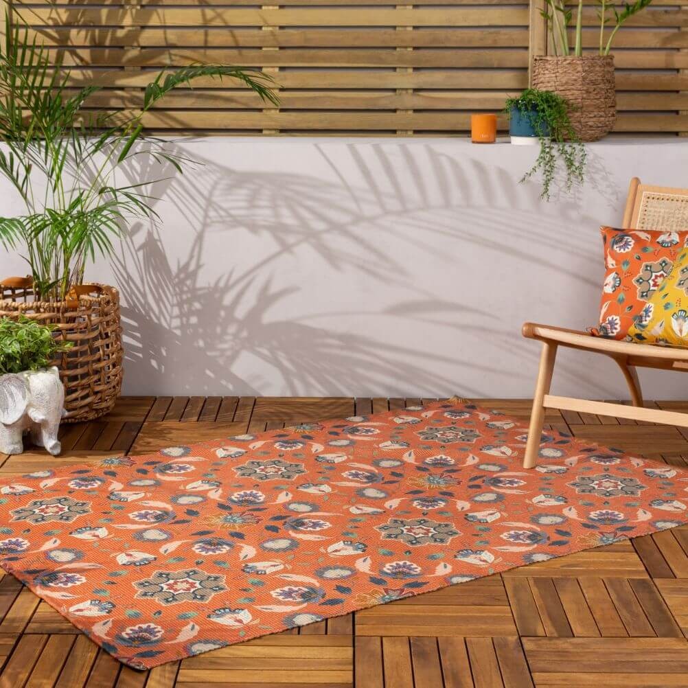 A decked outdoor space with an orange floral patterned rug in a folk art style. 