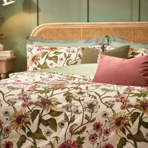 A floral duvet cover set with a pattern of flowers and vines growing across it. The bed is dressed with pink and green cushions.  