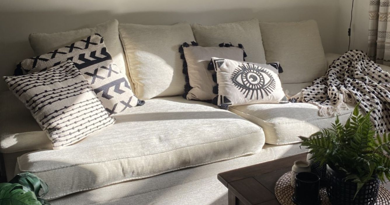 A plain cream coloured sofa in front of a neutral wall, decorated with black and white scatter cushions with striped, geometric and abstract designs, and a coordinating black and white throw.