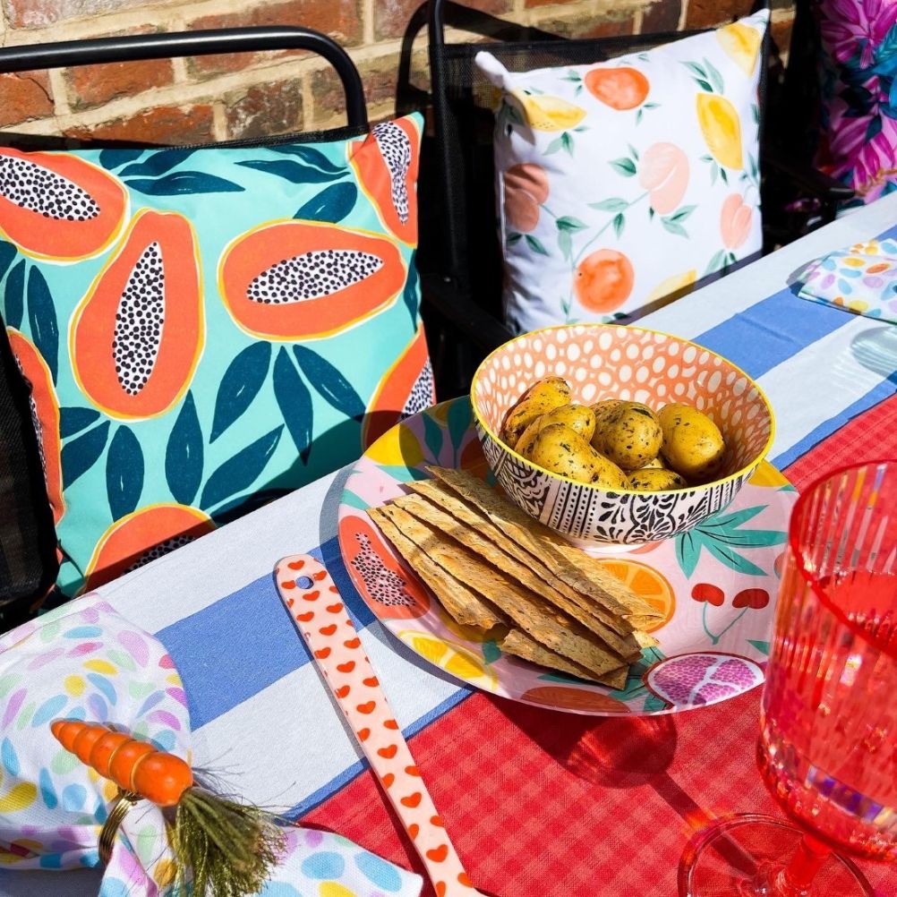 An outdoor table set up with brightly coloured and patterned cushions and bright table settings
