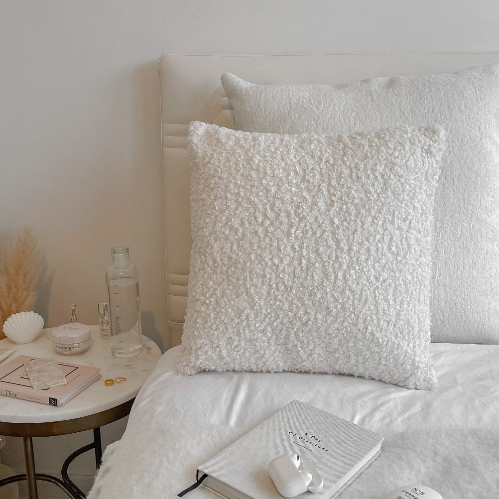 A white bed with a white duvet cover set and a white boucle cushion. 