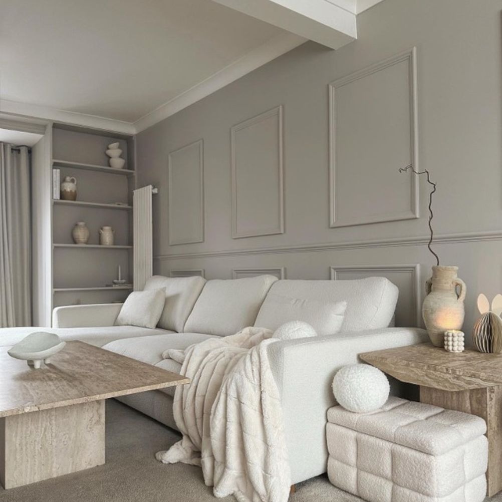 A minimal style living room with greige panelled walls, a white sofa and white throws and cushions.