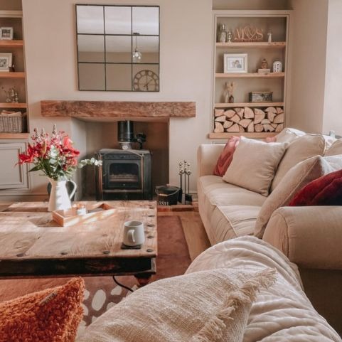 a country style living room with a wood-burner as a the focal point. On two cream sofas there are lots of cushions in cream and a gingery orange.