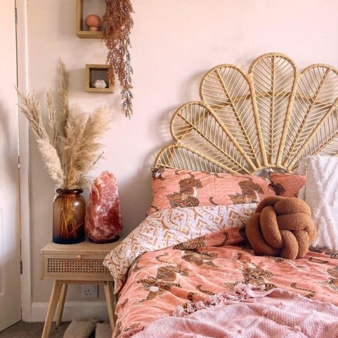 a boho style bedroom with a peacock rattan header, coral pink  bedding and a boucle knot cushion.