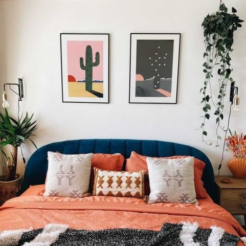 a western or cowboy style bedroom with cactus art prints, plants and a terracotta bedding set on the bed.