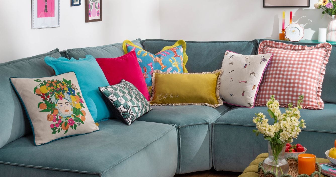 An arrangement of sofa cushions of various colours and designs, displayed on a muted blue sofa.