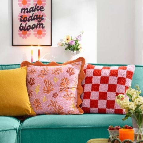 A teal sofa matched with a selection of three cushions in bright red, pink, yellow and muted orange shades.