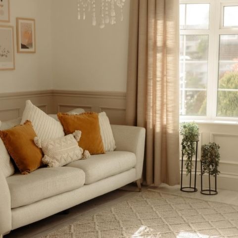 A cream 4-seater sofa with a layered selection of cushions in cream and saffron.