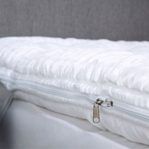 A close up image of a white polyester mattress topper, showing the zip opening.