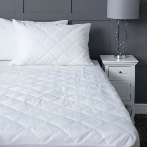 An undressed bed with a white diamond stitched antibacterial mattress protector, with two matching white pillows.