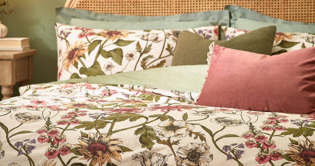 A closeup image of a floral duvet cover set with a traditional botanical design, made on a bed with coordinating green and pink throw cushions.