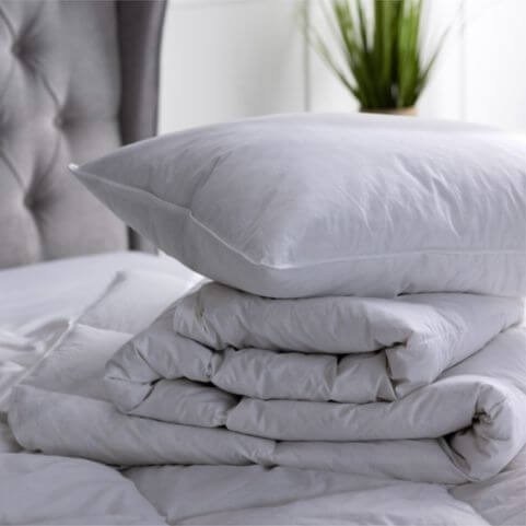 A luxury hotel quality quilt and pillow with duck feather filling, piled together on an undressed mattress.