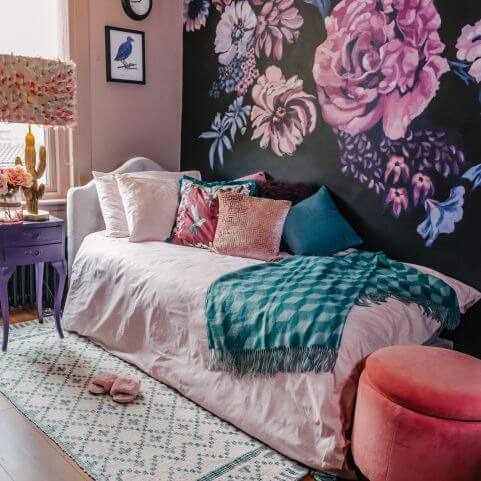 A single bed dressed with pink bedding, a selection of pink and blue scatter cushions and a bright blue geometric throw.