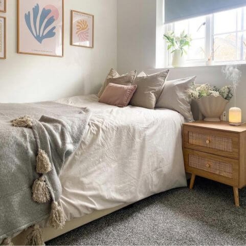 A small double bed dressed with off-white bedding, coordinating throw cushions and a grey tasseled throw.