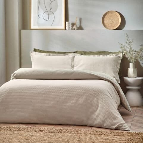 A waffle textured cotton duvet cover in an earthy beige shade, dressed on a bed with a green throw.