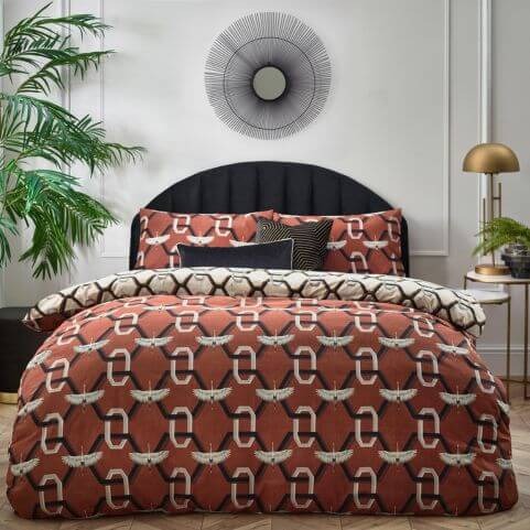 A brick red duvet cover set with a white crane and geometric chain link design, dressed on a bed with a two contrasting scatter cushions.