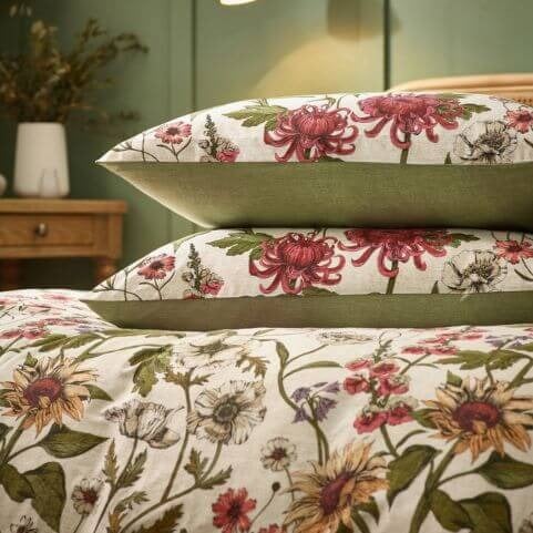 A percale cotton bedding set with a heritage botanical design and two matching pillowcases, arranged in a room with green walls and a decorated side table.