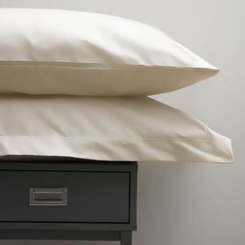 An Egyptian cotton pillowcase in an off-white ivory shade, placed on a black side table.