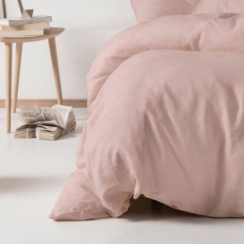 A linen duvet cover set in a pastel pink shade, arranged on a bed and sweeping the floor for a luxurious effect.