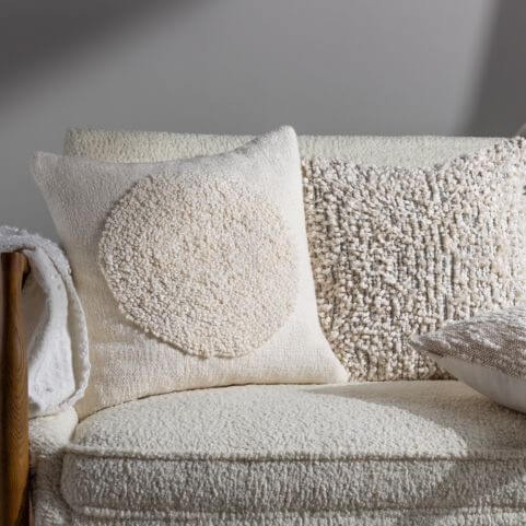 A selection of white bouclé cushions arranged on a white bouclé sofa with a coordinating throw blanket.