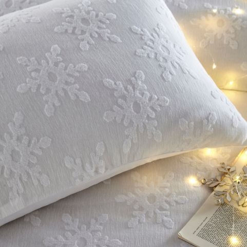 A closeup image of festive bedding with a white tufted snowflake design, made on a bed with decorative fairy lights.