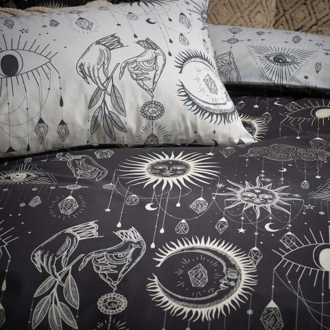 A monochrome duvet cover set with a printed galaxy and mystical symbol design, made on a bed with contrasting pillowcases.