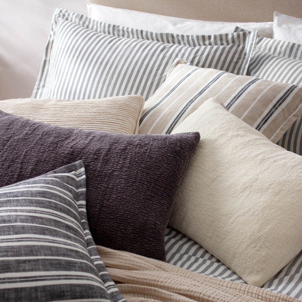A bed with a navy blue striped duvet cover, striped cushions and fleece rectangle cushions