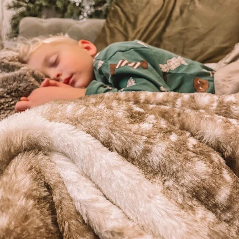 A child sleeping on a sofa, cuddled up with a brown and white coloured faux fur throw.
