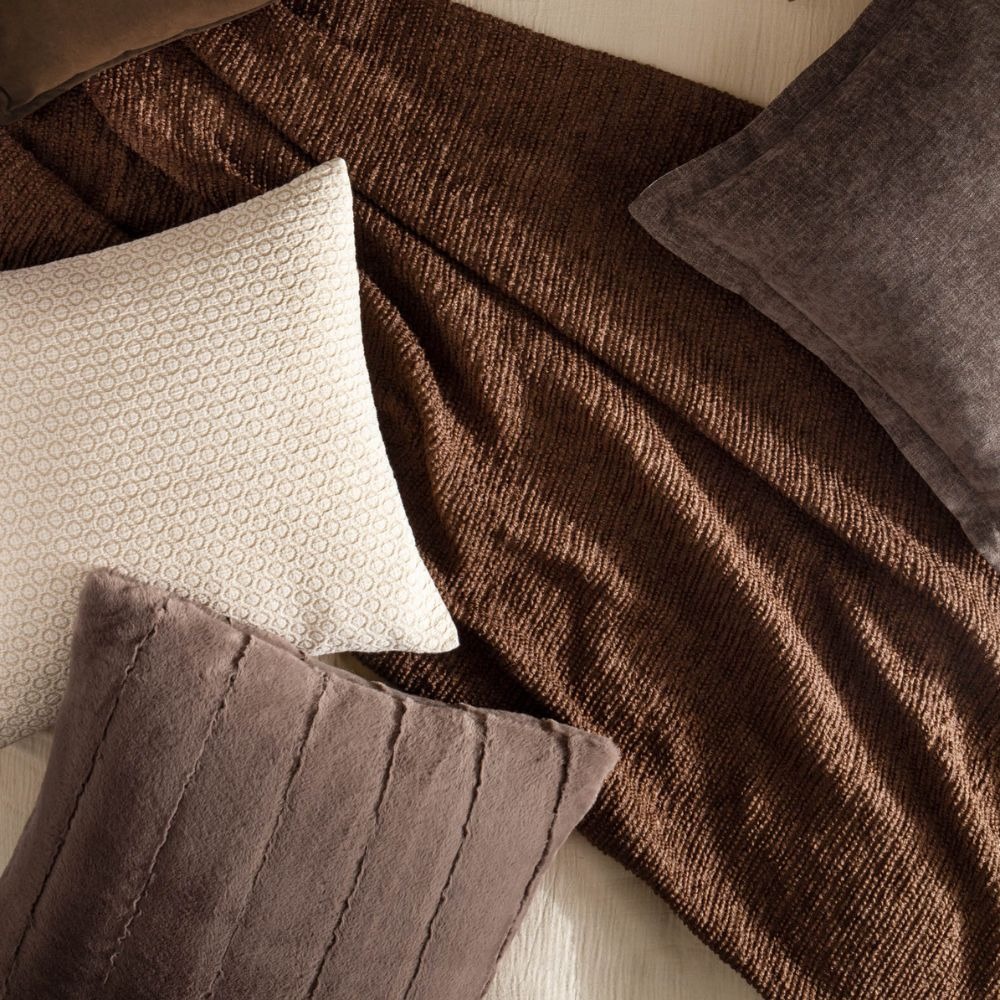 A collection of brown homeware featuring a brown throw, brown faux fur cushion and a cream cushion