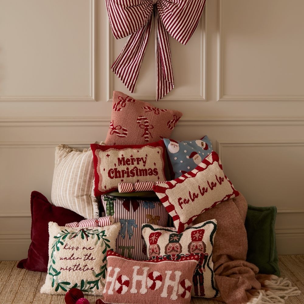 A collection of festive cushions stacked up on top of each other with a red striped bow at the top